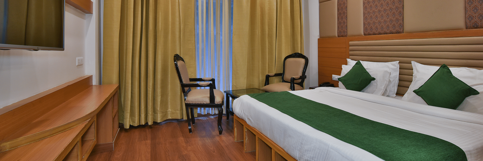 A large bed placed next to two chairs in the Deluxe Room at DLS Highland Resort and Spa, Mussoorie.